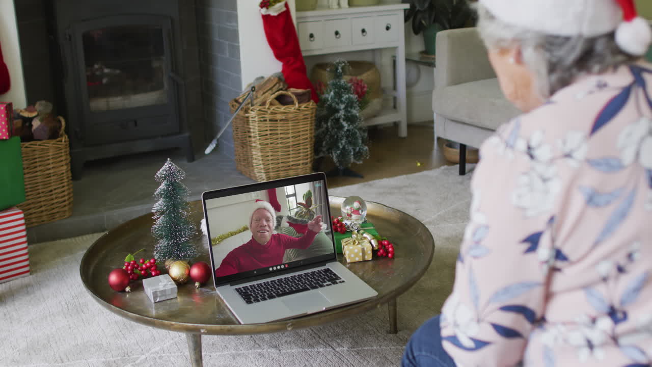 mujer mayor caucásica usando una computadora portátil para una videollamada de navidad con un hombre sonriente en la pantalla