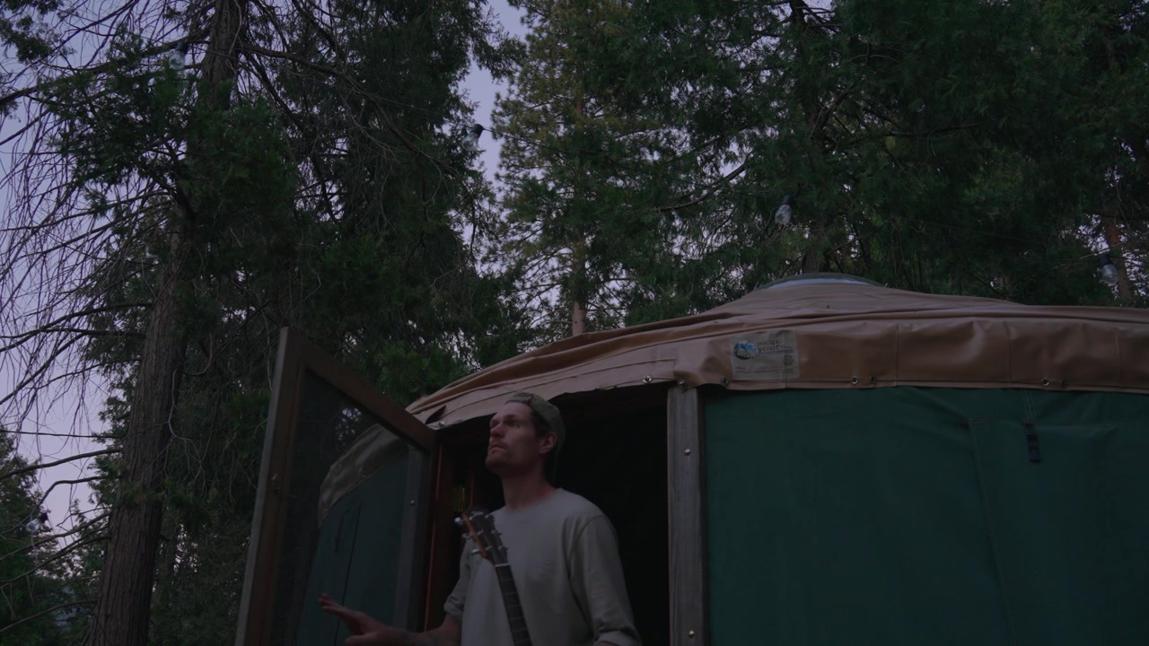 Un uomo esce da una tenda yurta di tela in un campeggio nel bosco al tramonto