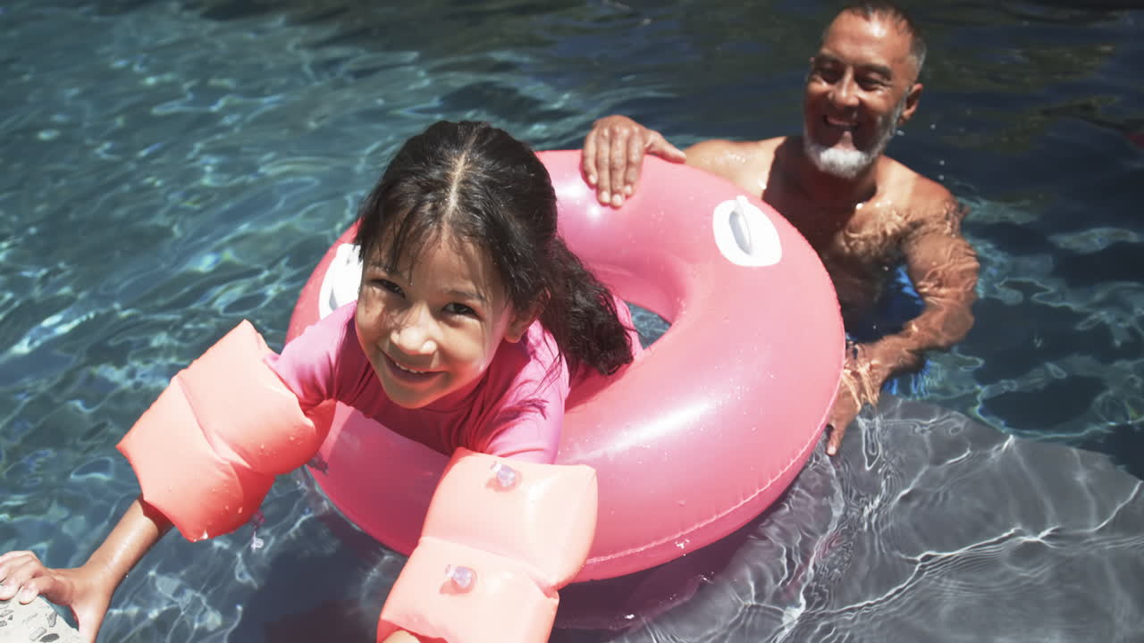una chica biracial con brazos flotantes disfruta del tiempo en la piscina con su abuelo