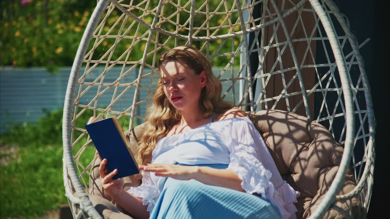 Gravid kvinde læser en bog og slapper af i en æggestol udendørs