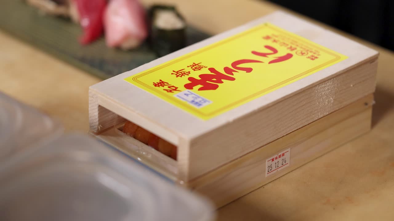 Close-up shot of hands opening a traditional wooden box containing fresh orange sea urchin
