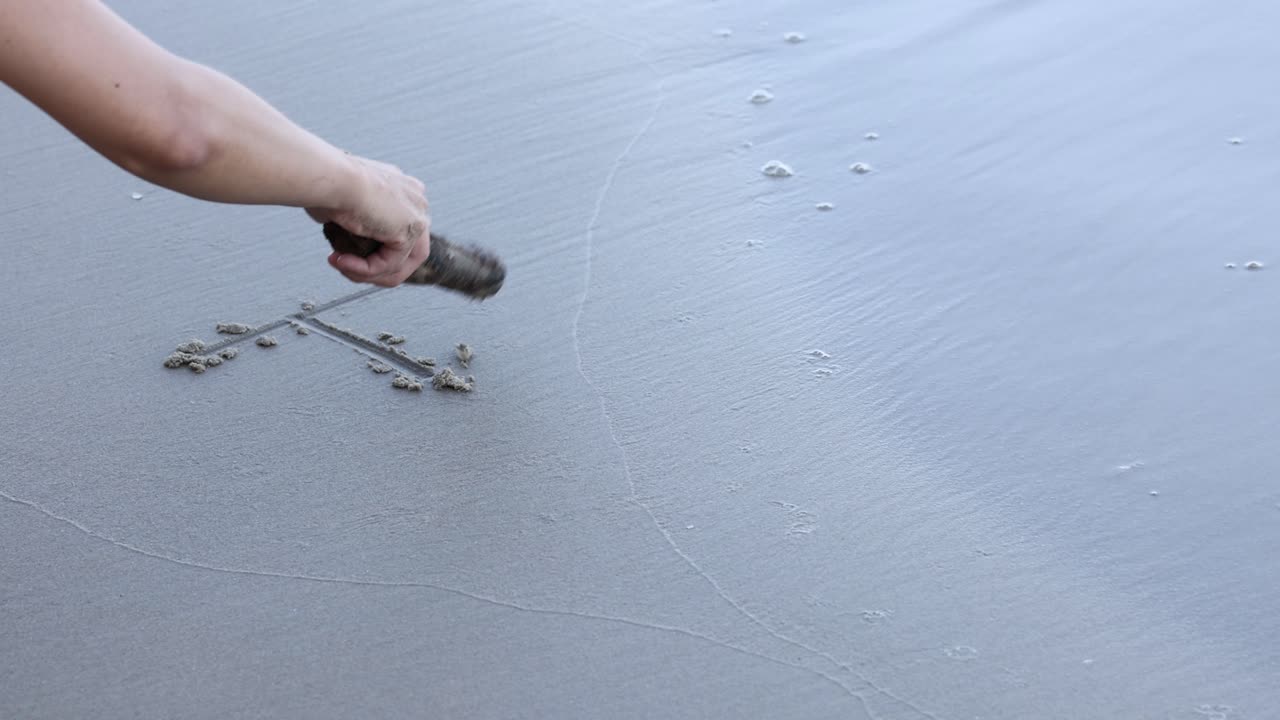 Hand inscribing \'Hi\' on sandy beach surface.
