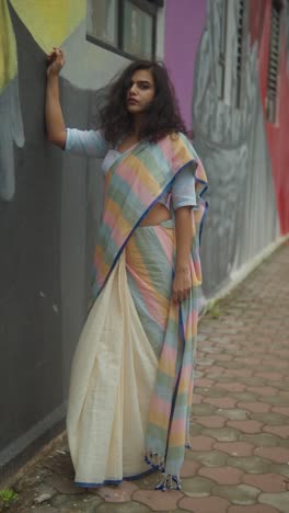 indian model in pastel saree poses confidently against an urban mural wall for a street-style fashion shoot