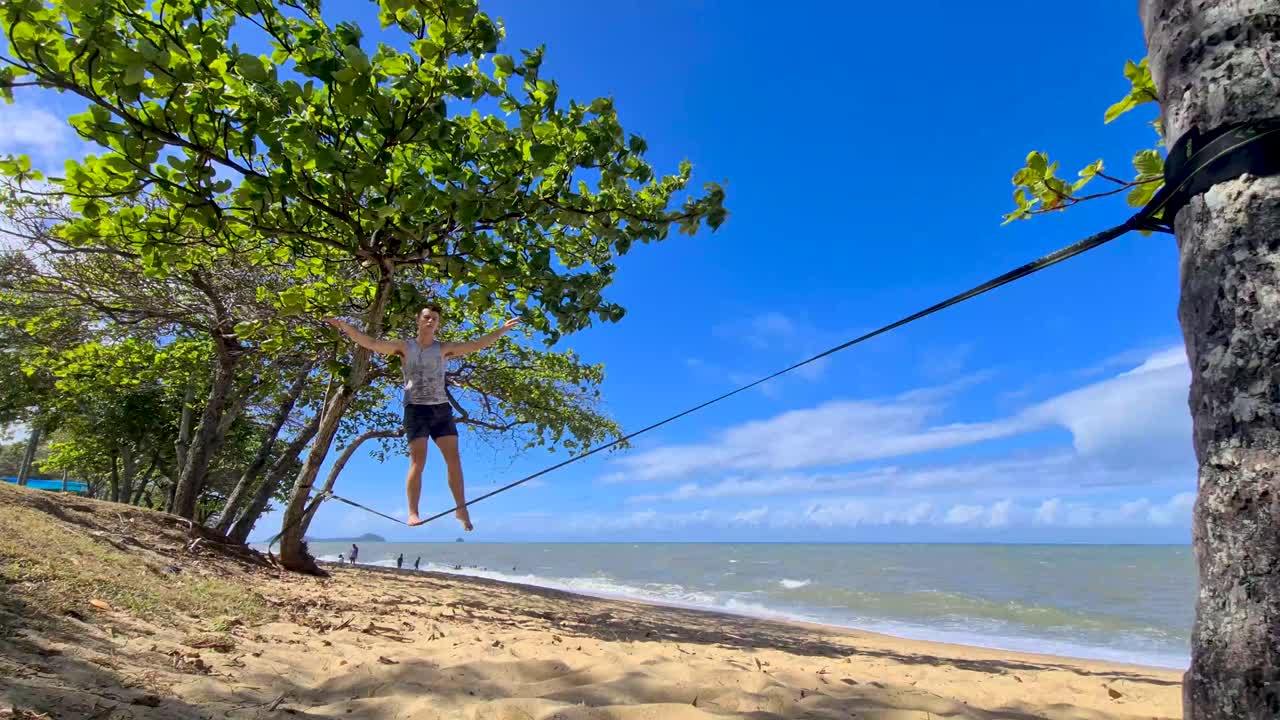macho adulto subiendo a slackline y equilibrándose en trinity beach en cairns