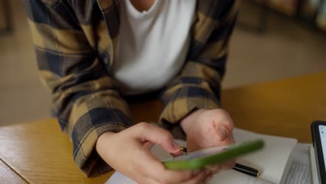 Close-up,-a-girl-in-a-white-T-shirt-and-a-plaid-shirt-sits-at-a-table-and-types-on-her-smartphone