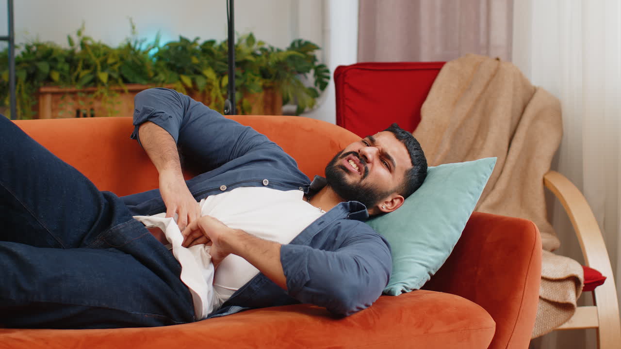 hombre indio acostado en el sofá sensación repentina fuerte dolor de estómago gastritis envenenamiento diarrea