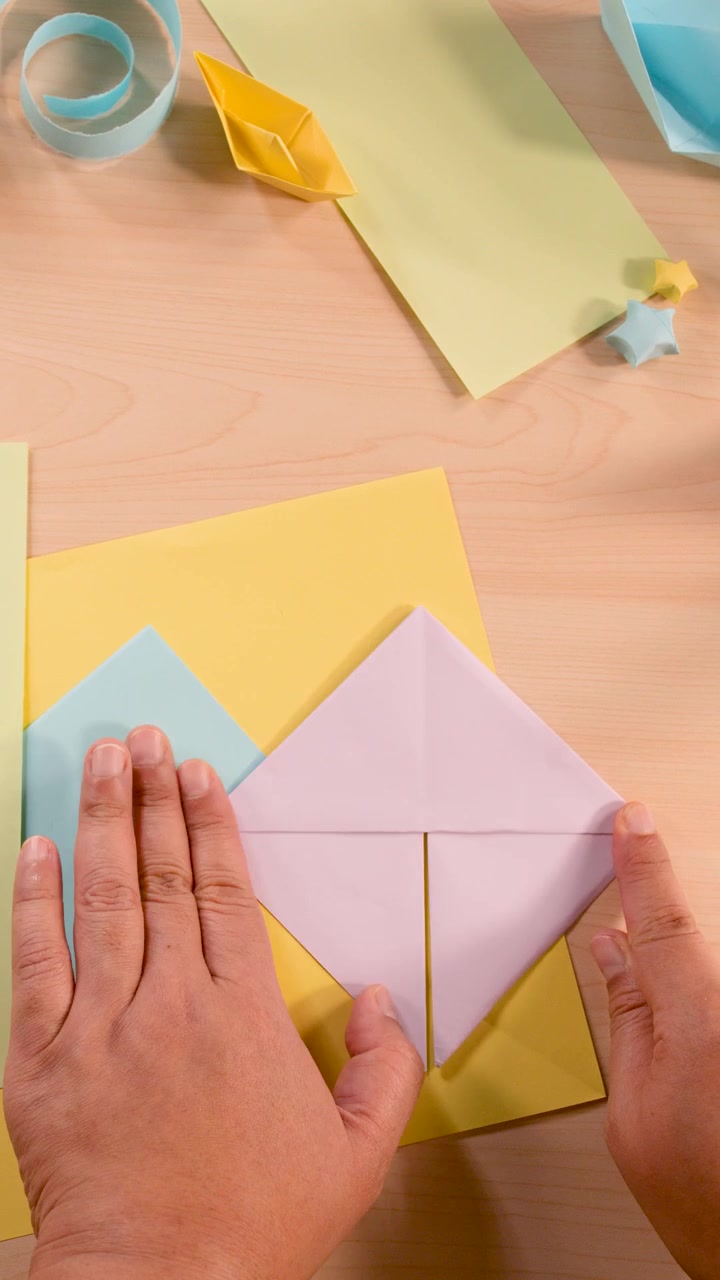 Una persona piega carta origami pastello, vista dall'alto, illuminazione soffusa, materiali per lavoretti colorati, telecamera stabile