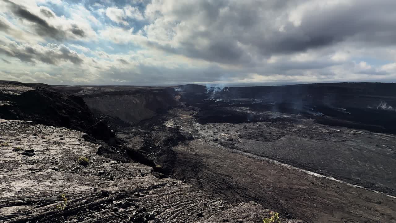 Ampia vista statica del cratere Kīlauea sulla Grande Isola delle Hawaii, che mostra vasti campi di lava e leggero fumo vulcanico che si sposta attraverso la caldera sotto un cielo nuvoloso