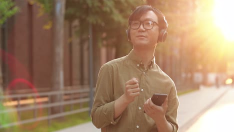 asian student man wearing glasses dancing and listening to the music on smartphone in the street