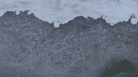 a frozen lake with intricate ice patterns and snow patches, aerial view