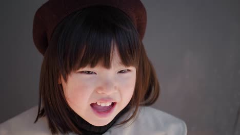 회색 코트와 모자를 입은 한국 소녀는 가게의 유리 문에서 봄에 거리에 서 있습니다.