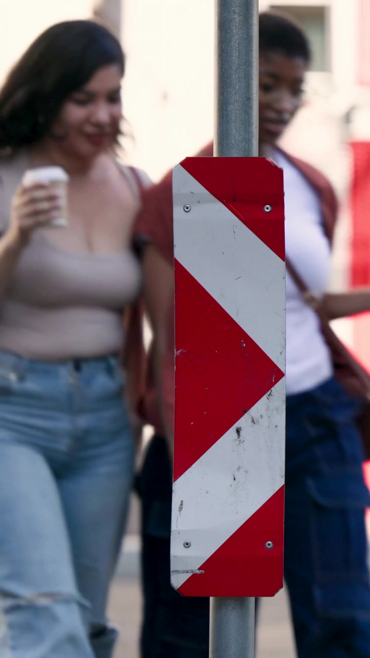 Vertical video: Passing man from left starting on curb, chevron plate centered, phone and cup seen