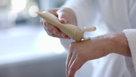applying lotion, mature woman in bathrobe moisturizing hands at home