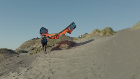 hombre caminando por el camino de la playa sosteniendo una vela de kite surf en un día soleado y ventoso en matanzas, chile