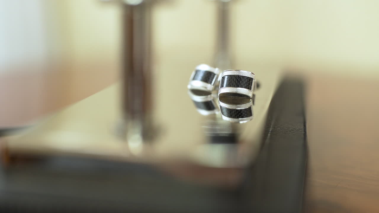 Abotoaduras Elegantes Prateadas e Pretas em Superfície Reflexiva