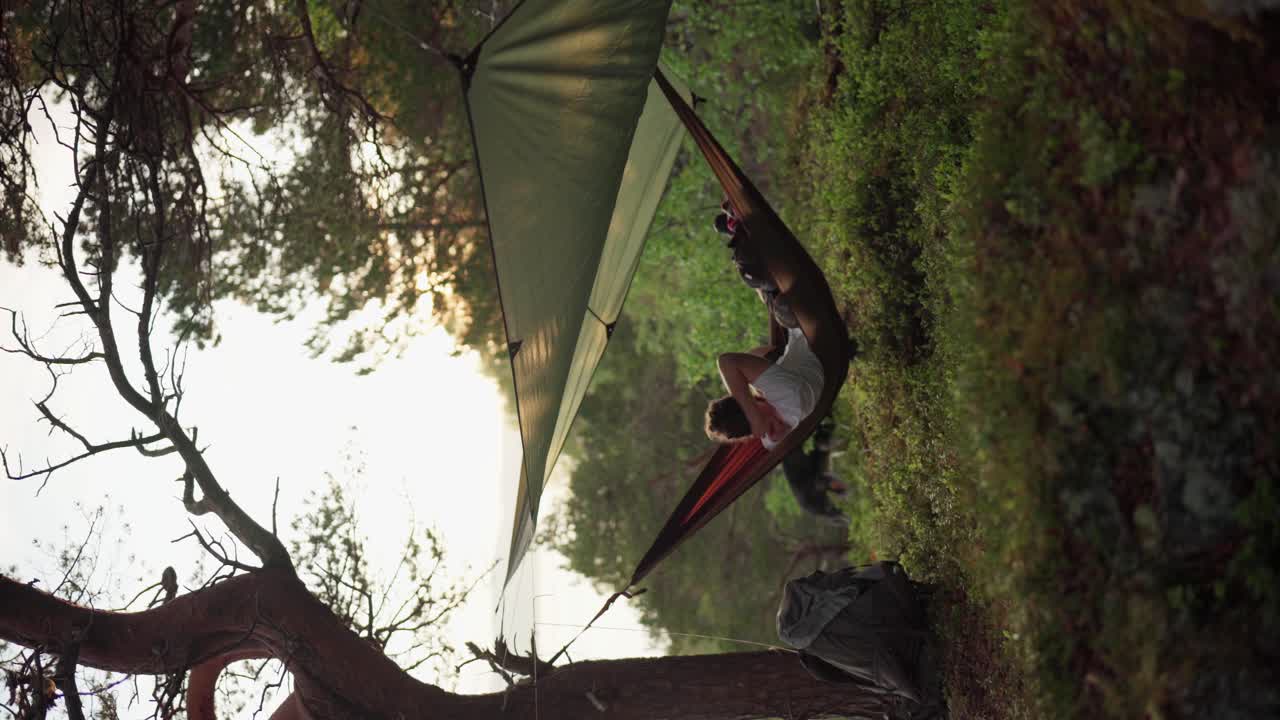 나무에 매달린 해먹에 누워 스윙하는 젊은 남자의 세로 샷