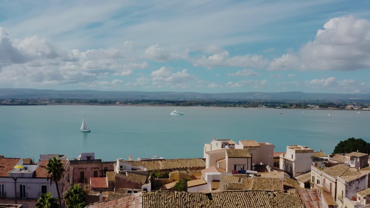 Flying above historic buildings on the island of Ortigia with yacht and boats in the Mediterranean sea. Aerial drone shot of medieval old town in Syracuse, Sicily.