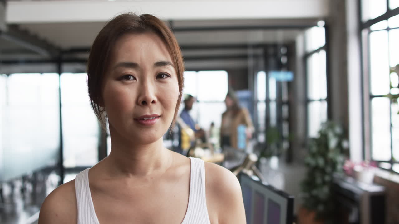 Middle-aged Asian woman standing in front, diverse team discussing in background