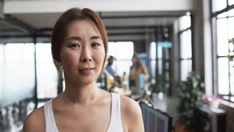 middle-aged asian woman standing in front, diverse team discussing in background