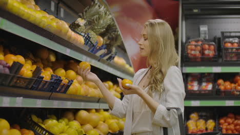 Slow-motion-girl-chooses-tangerines-puts-into-bag.-Slow-motion-close-view-girl-hand-chooses-fresh-aromatic-tangerines-and-put-into-plastic-bag-against-boxes