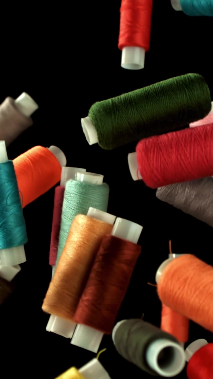 Colorful Thread Spools Falling Against Black Background
