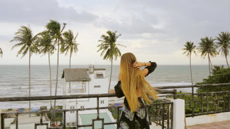 female model on vacation walks across balcony with magnificent views of the beach and palm trees in background