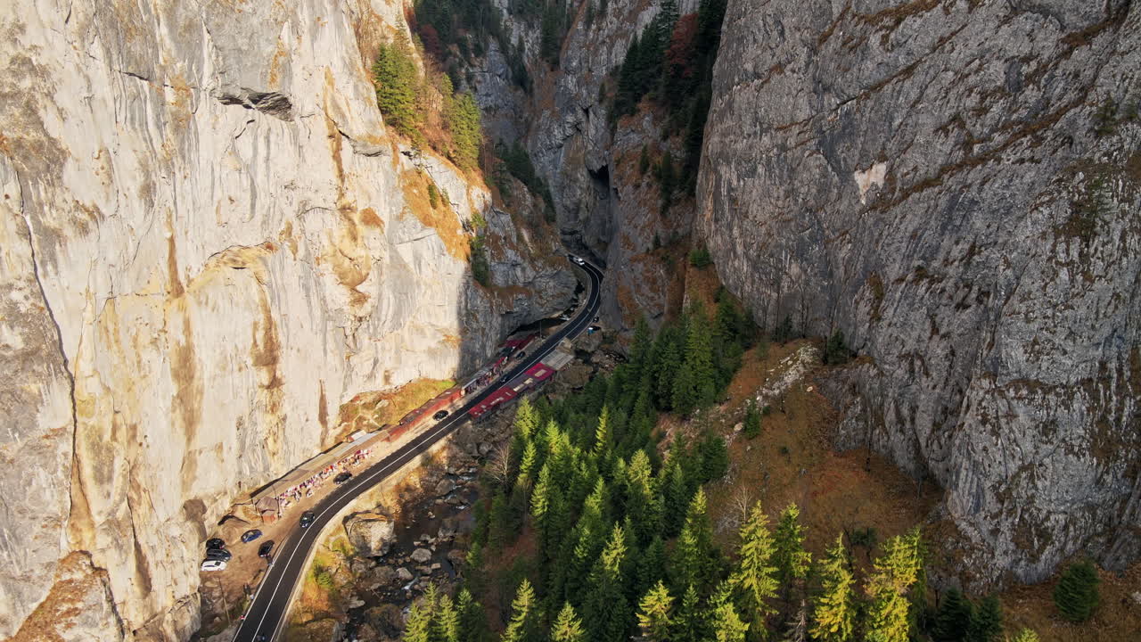 Aerial drone view of nature in Romania. Carpathian mountains, road with cars in the valley, rocky cliffs, lush forest, river