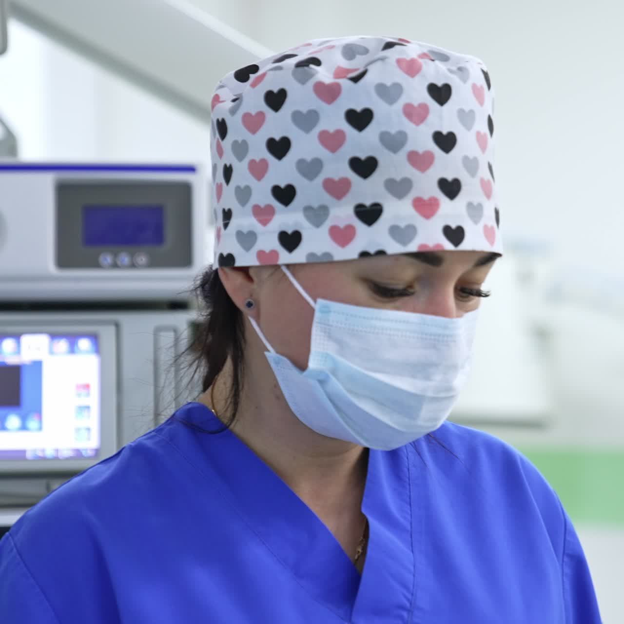 Good-looking female nurse in cap and mask standing in modern hospital. Advanced equipment at backdrop in blur
