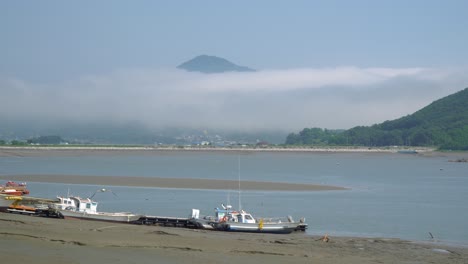 Barcos-De-Pescadores-Atascados-En-El-Barro-Durante-La-Marea-Baja-En-La-Isla-De-Ganghwado-En-Corea-Del-Sur,-Neblina-Y-Vapor-Sobre-Los-Picos-De-Las-Montañas