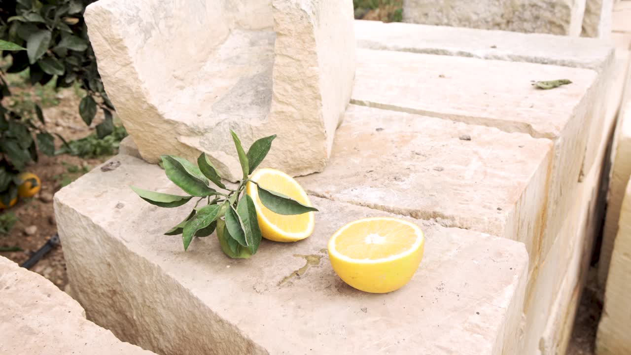A vibrant lemon cut in half rests on rustic Maltese limestone, accompanied by green leaves, capturing the freshness and agricultural charm of Mediterranean citrus harvest.