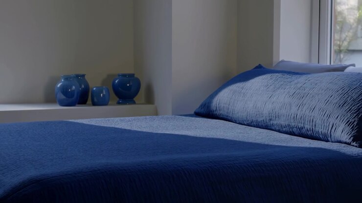 Letto blu con vasi in ceramica sul davanzale, piumino e cuscino in lino testurizzato, arredamento moderno minimalista, allestito