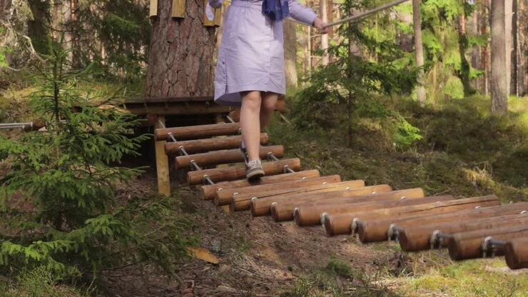 Nainen arkivaatteissa kävelemässä vaarallisen puisen riippusillan yli.