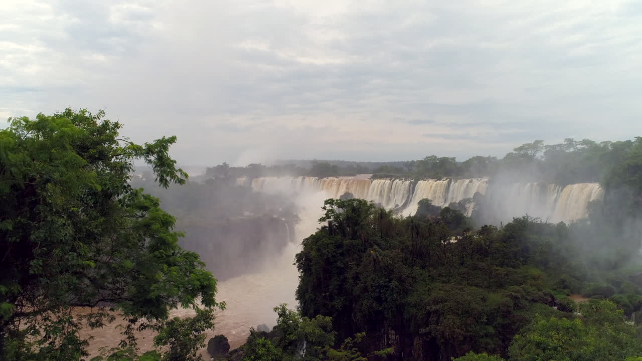 un avión no tripulado emergiendo de detrás de los árboles, revelando las impresionantes cataratas de iguazu