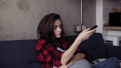 una joven atractiva morena cambia de canal de televisión con el control remoto hasta que encuentra algo que le gusta ver.