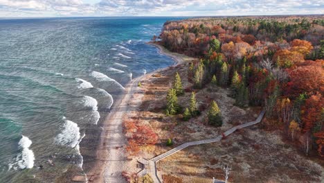 golden autumn shoreline along lake superior’s upper peninsula, captured by drone with breaking waves and a forest-lined trail curving through the scene
