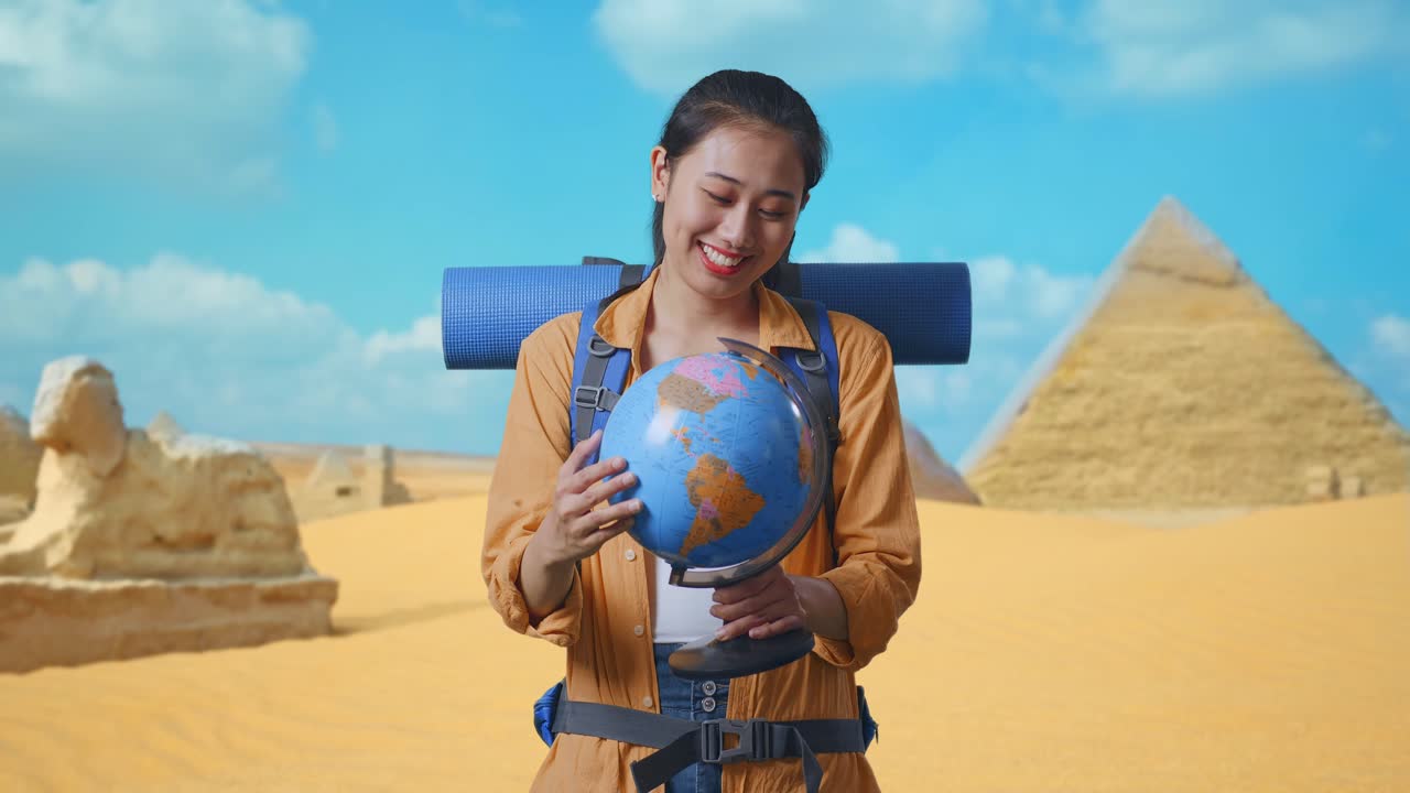 Asian Female Hiker With Mountaineering Backpack Holding World Globe In Her Hands And Smiling To Camera While Traveling In Pyramid Of Giza