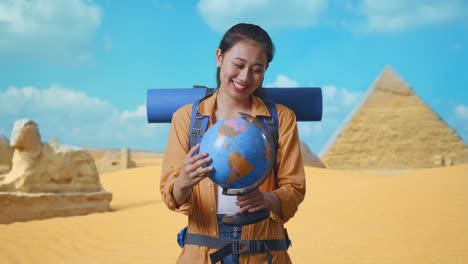 asian female hiker with mountaineering backpack holding world globe in her hands and smiling to camera while traveling in pyramid of giza