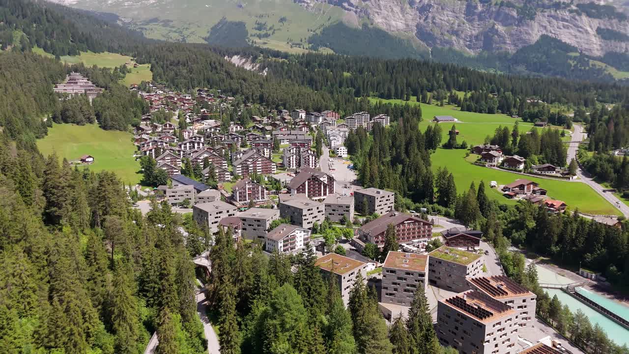 Aerial wide shot of Swiss town with apartment blocks in small city of Laax, Switzerland. Sunny day in summer. Forest trees and homes in valley