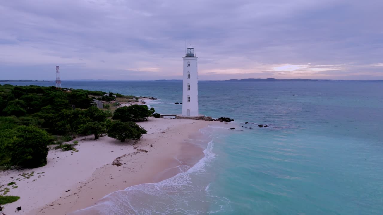 Lighthouse in idyllic white sand beach with crashing aqua blue sea waves, drone reveal shipwreck on east Sri Lanka coastline.