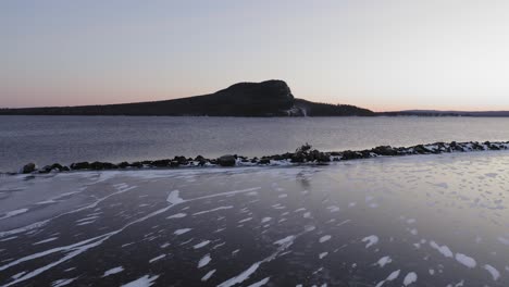 slow push towards rocky breakwater with a mountain on the other side of lake aerial