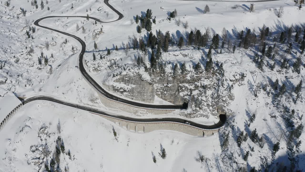 Cars navigate winding Falzarego mountain pass in white Italian Dolomites winter landscape Aerial