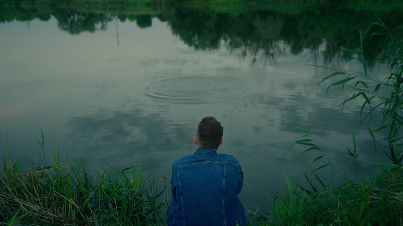 Man Throwing Rock into Calm Lake at Dusk