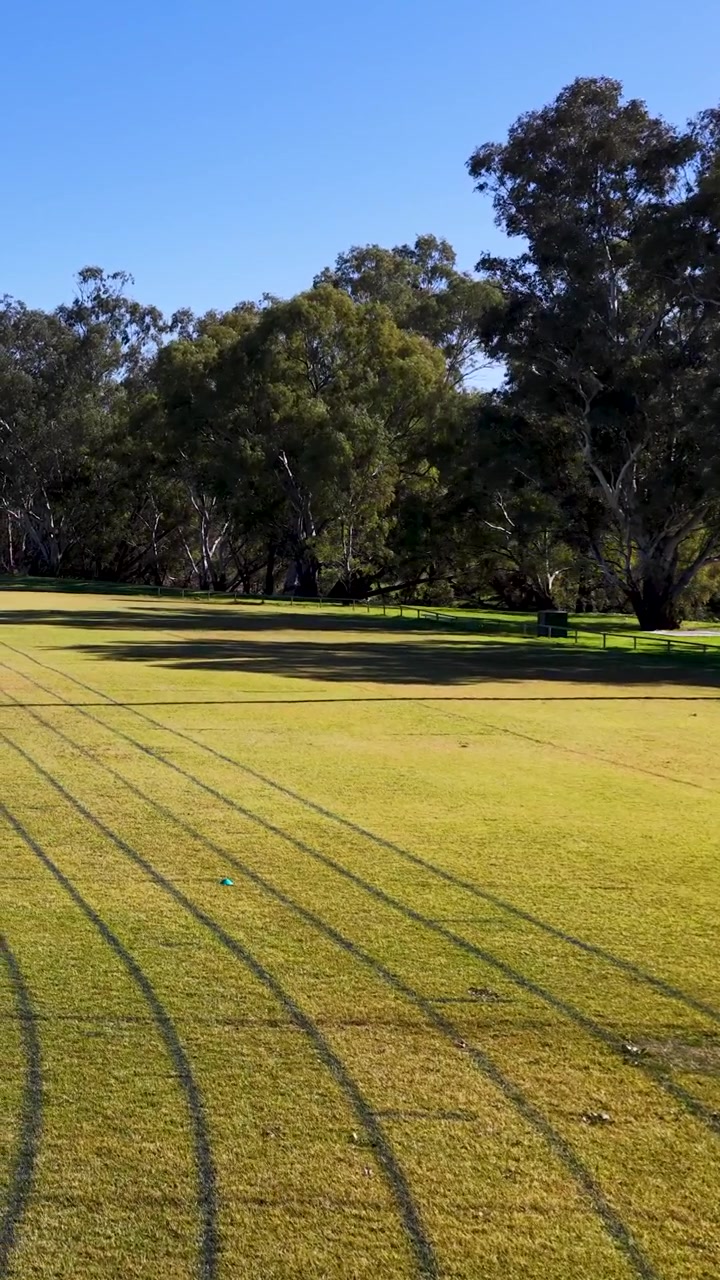 Inquadratura ampia di una pista da corsa in erba curva sotto la luce solare intensa a Gunnedah, Australia.
