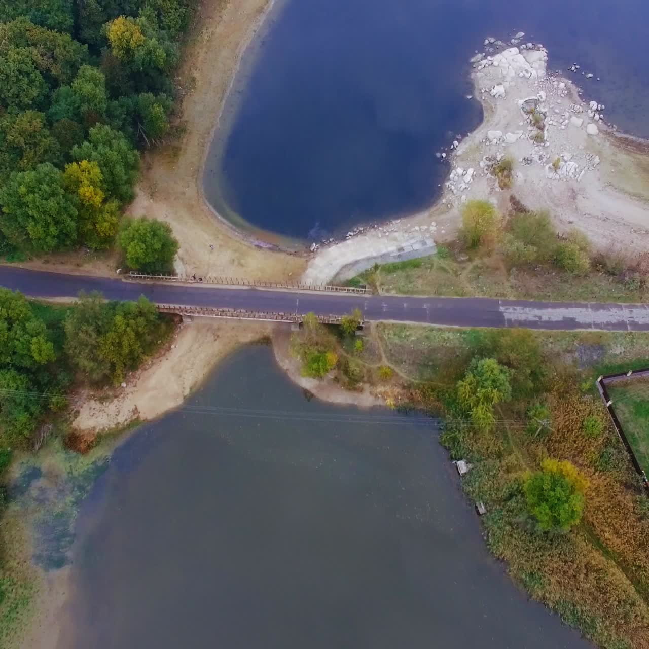 Flight over the river locating in the rural area. Houses and trees locating on the waterfront. Grey autumn day top view