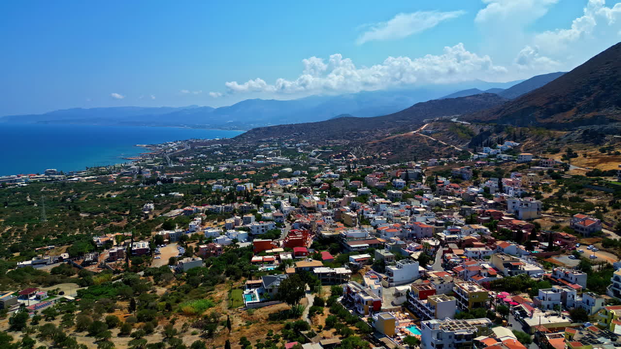 Aerial panorama establishing Piskopiano, Greece, coastline with homes mixed between greenery at base of mountains