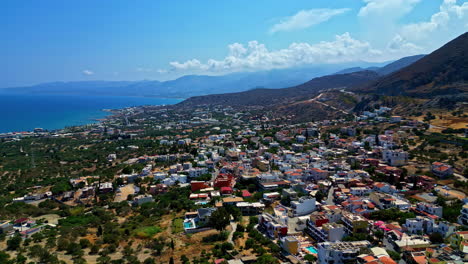 aerial panorama establishing piskopiano, greece, coastline with homes mixed between greenery at base of mountains