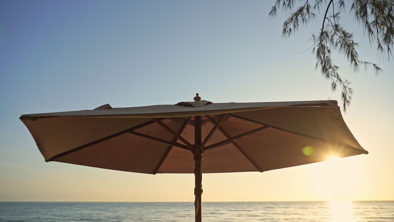 una sombrilla en la arena de la playa cerca del reflejo del sol en el agua del mar durante una puesta de sol soleada