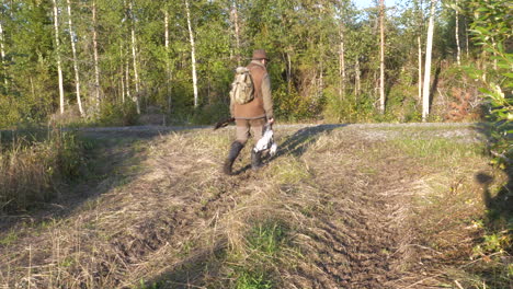 successful hunter walking on forest road carrying birds and rifle, a hunting day's reward