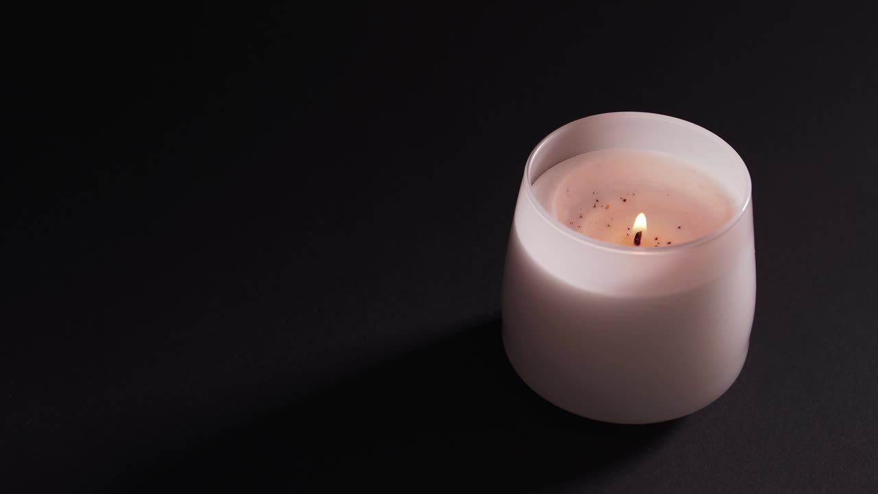 A white burning candle in a glass is isolated against a dark background. Relax and aromatherapy, the concept of faith and hope 4k