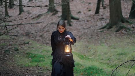 mujer de negro caminando a través de un bosque espeluznante con una lámpara de aceite iluminando el camino